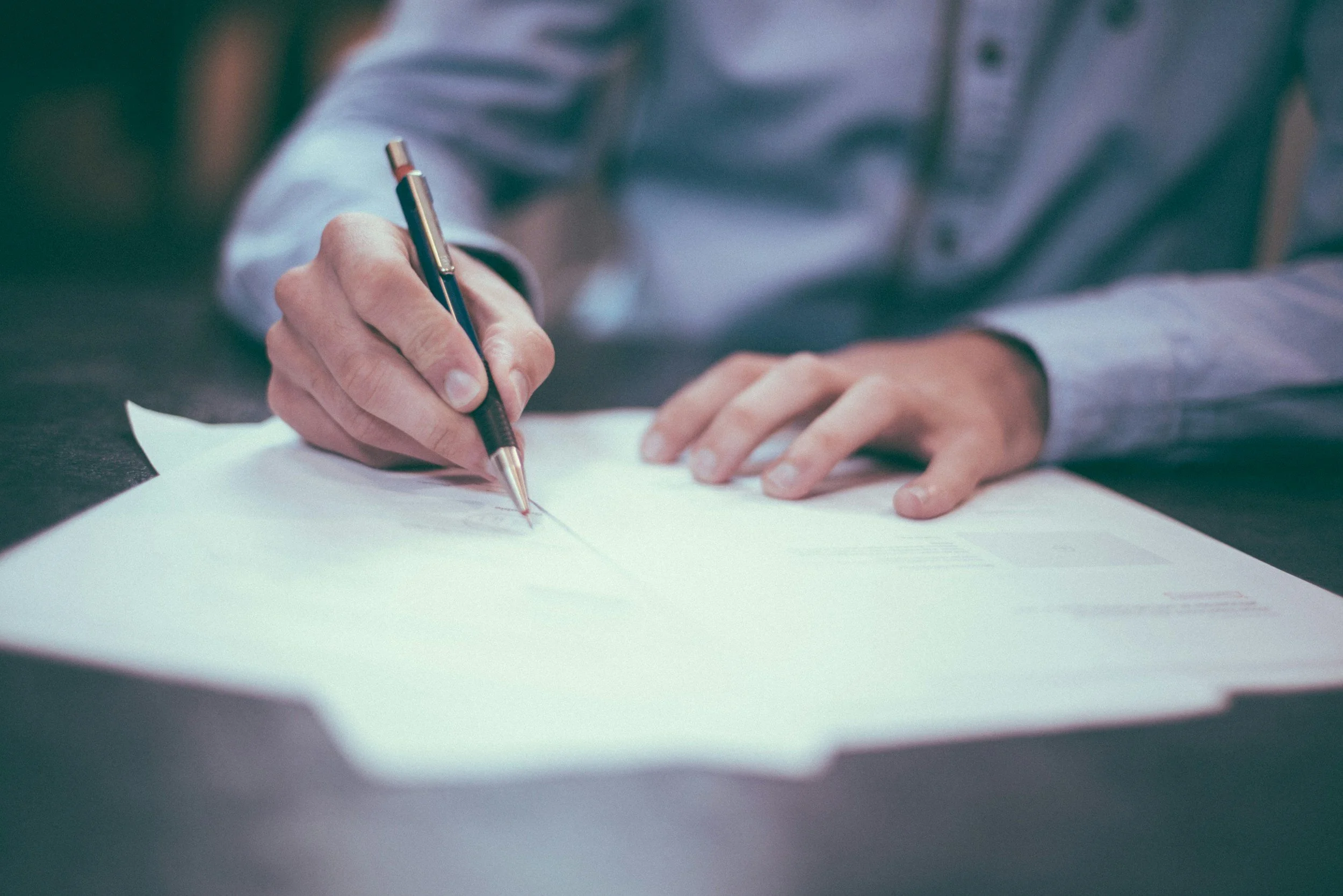 Close-up of a person writing on a piece of paper with a black pen, wearing a striped shirt.