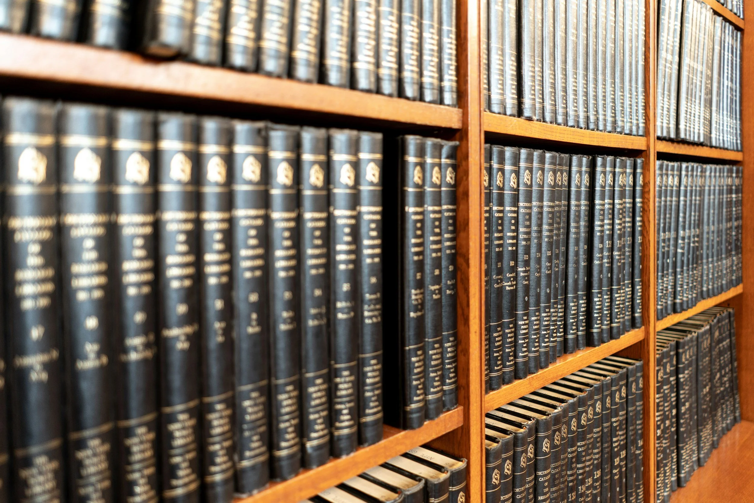 Close-up of wooden bookshelves filled with numerous black hardcover books with gold lettering.