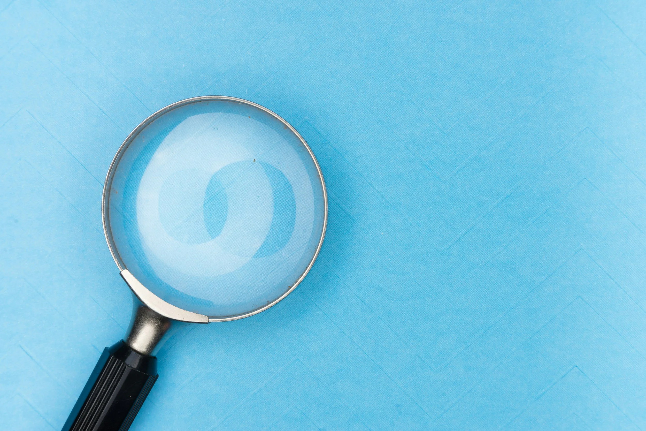A magnifying glass with a black handle and silver rim placed on a light blue background.