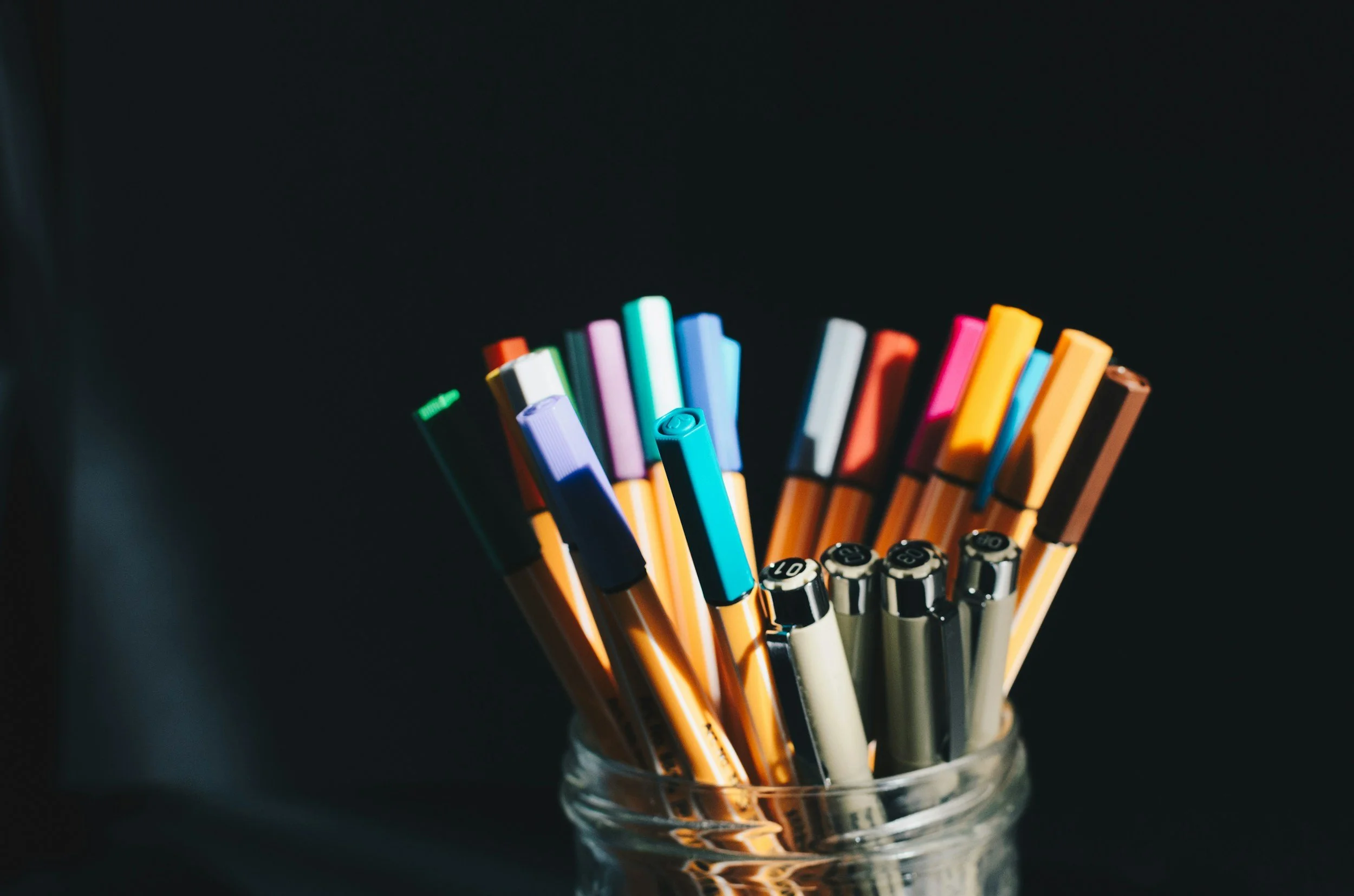 Colorful markers in a glass container on a dark background.