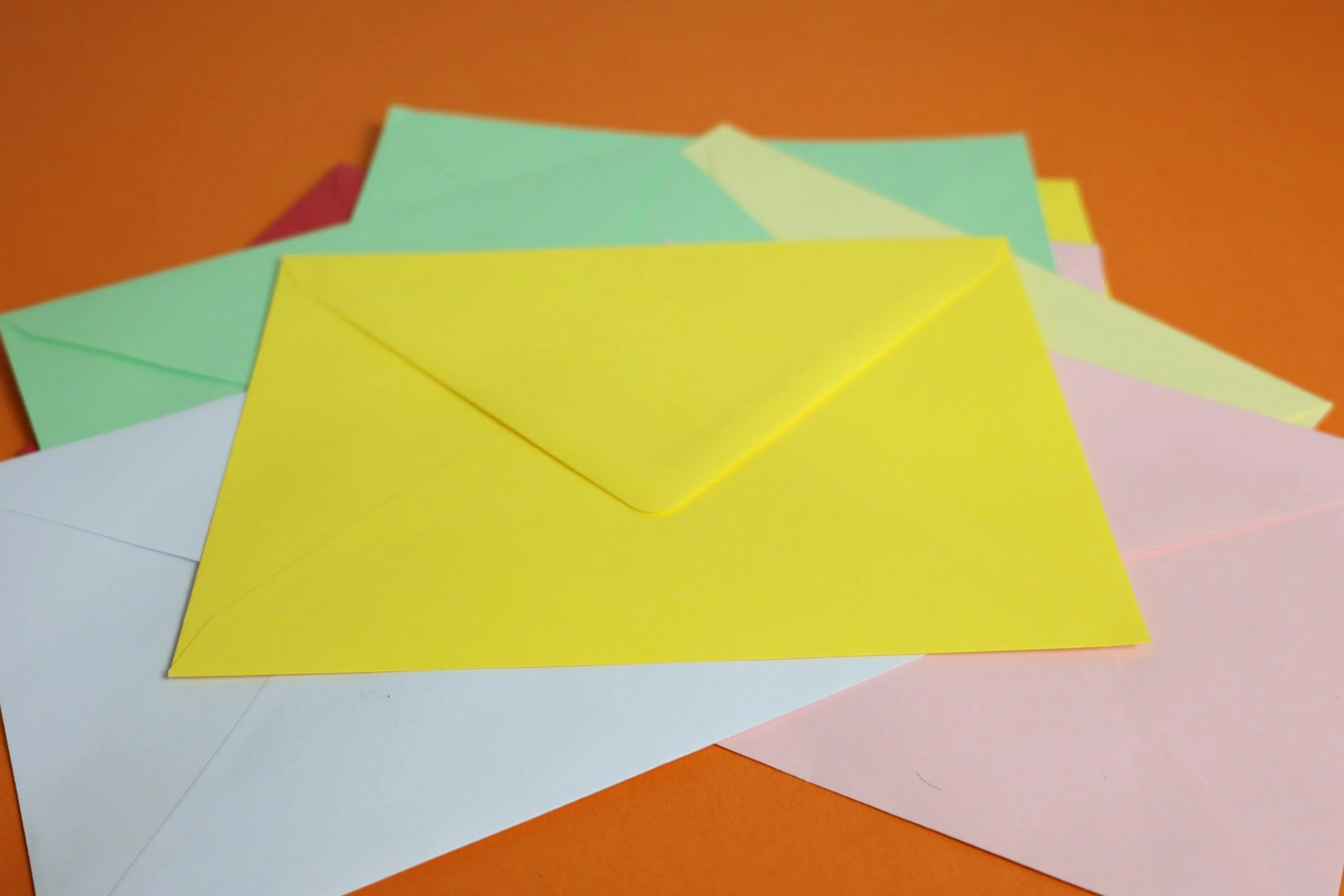 Colorful paper sheets in yellow, pink, green, and white stacked on an orange surface.